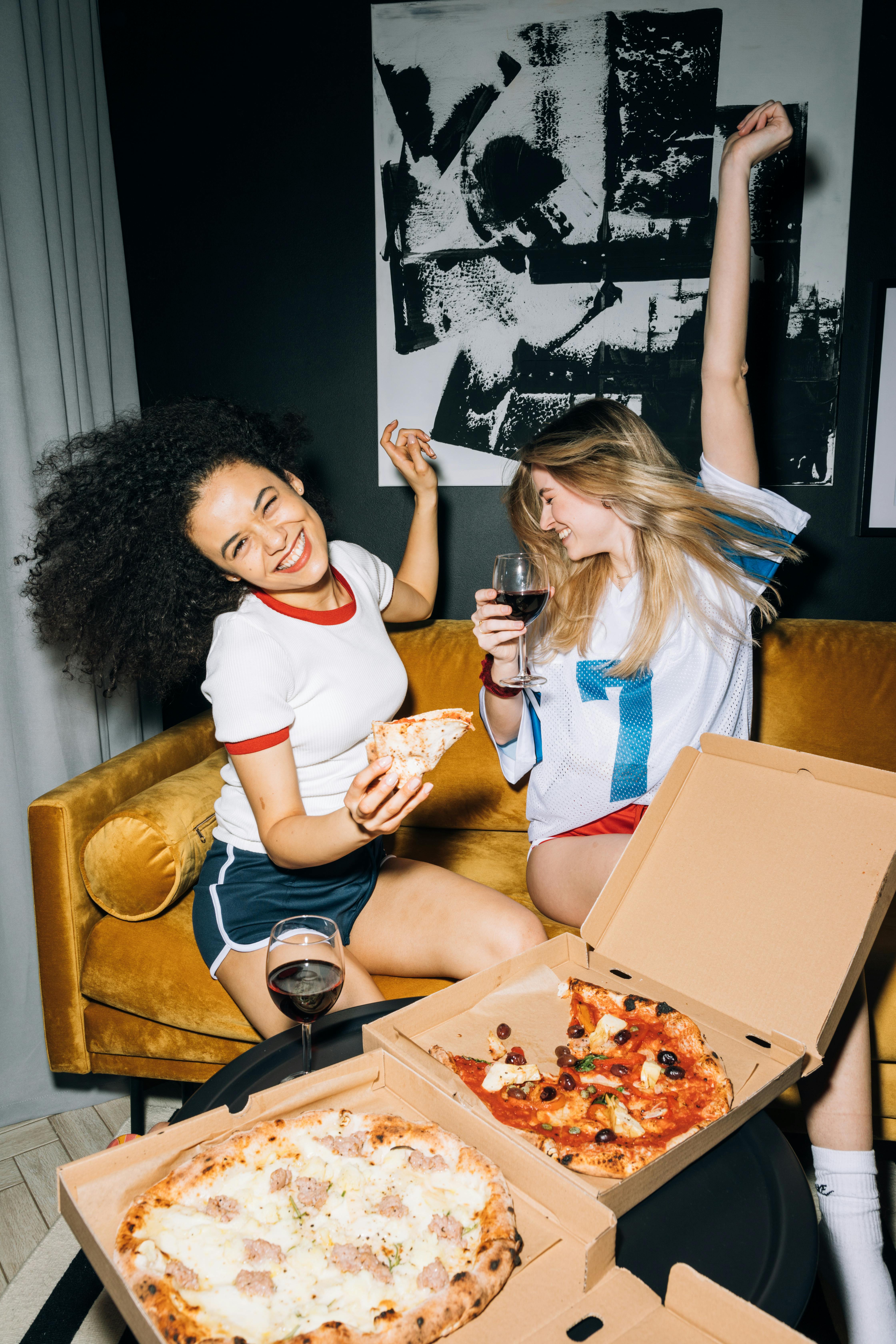 two girls having fun with drinks and pizza